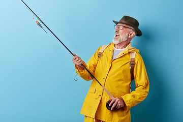 crazy funny smiling old fisheman enjoying hobby, close up photo. isolated blue background, copy space, happiness