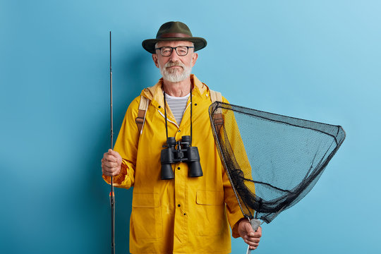 bearded good looking old man holding fish tank and rod preparing for fishing. close up photo. isolated blue background, studio shot