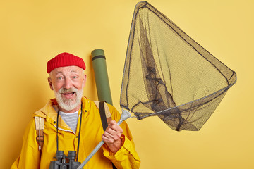 excited happy old man in red cap and yellow coat holding fishnet going to catch fish. favourite...