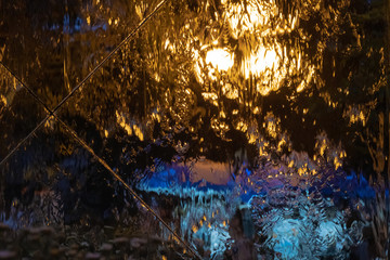 Multi-colored abstraction: water flowing down the glass with reflection of night lights.