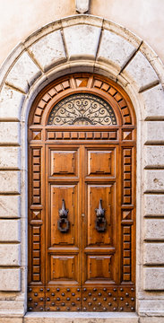 An ancient wooden portal with iron knocker, arch and window with metal decorations. Stone and marble frame. Italian craftsmanship. In an Italian city.