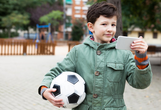 boy holding soccer ball and smartphone outdoors