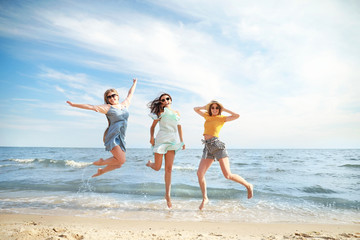 Happy jumping young women on sea beach at resort