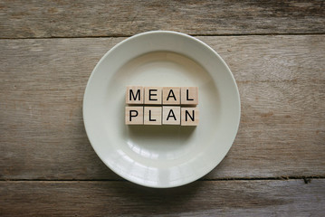 Wooden cube written with 'MEAL PLAN' on plate on wooden background. Food and diet concept.