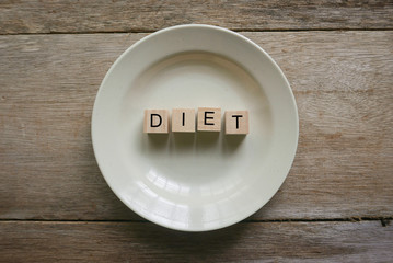 Wooden cube written with 'DIET' on plate on wooden background. Food and diet concept.