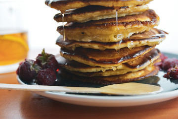 Pancake with dripping honey on a blue plate with raspberries