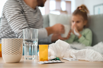 Medicines on table and blurred father taking care of his sick daughter on background