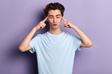 Naklejka premium young relaxed man holds fingers on temples, has bad memory, tries to concentrate and remember details of accident. meditation, free time, health care, lifestyle , isolated blue background, studio shot