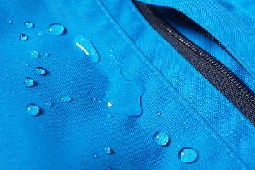 Closeup of water drops on bright blue fabric and black zipper with waterproof design to protect...