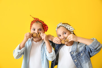 Portrait of funny twin girls with cookies on color background