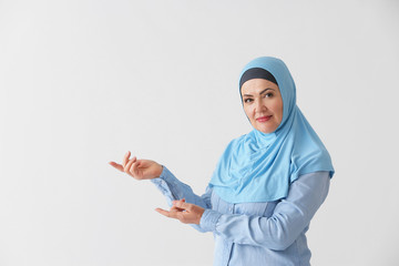 Beautiful mature Muslim woman showing something on light background