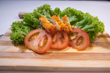 close up of slices of tomato,slices of fried chicken and salad on a wooden cutting board