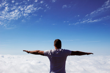 young man with open arms raised above the clouds