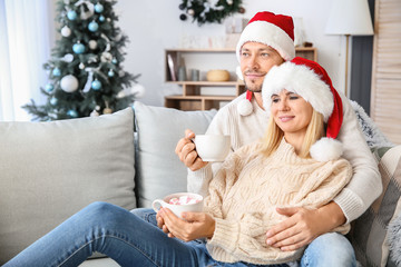 Obraz na płótnie Canvas Happy couple drinking hot chocolate at home on Christmas eve