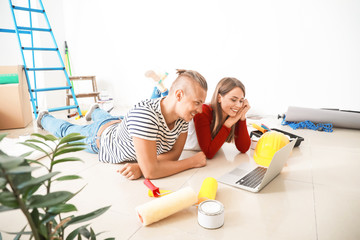 Happy young couple with laptop planning repair in their new house