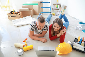 Happy young couple with laptop planning repair in their new house