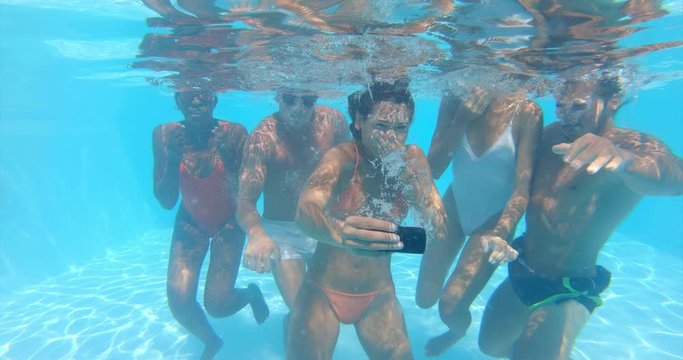 Underwater shot of young multi-ethnic friends in swimwear are having fun to enjoy their summer vacation and making selfie in swimming pool in a sunny day.