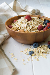wooden bowl with oatmeal and blueberries and raspberries on a white table next to a light brown napkin