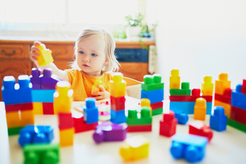 Little girl playing with colorful plastic construction blocks