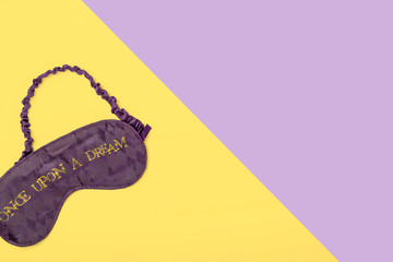 Purple satin  sleeping mask on yellow and purple background with space for text. Minimal flat lay concept.