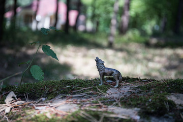 Howling wolf in the forest. Mini wolf figure standing on the forest ground.