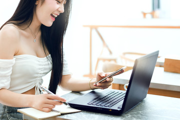 Beautiful Asian girl celebrate success and happy pose with good news from smartphone or laptop