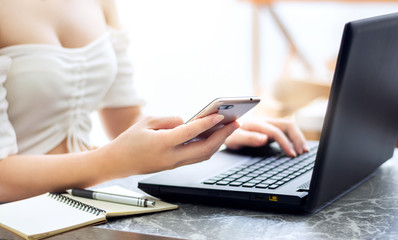 Closeup of hand asian woman using smartphone and laptop working online on desk