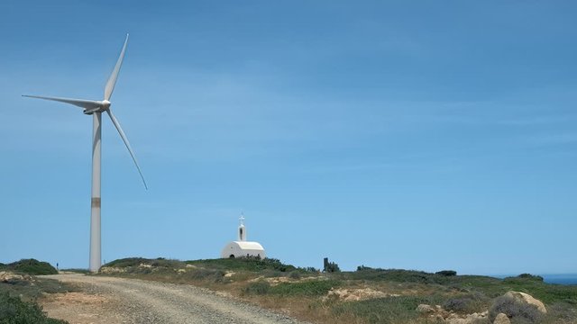 Single wind turbine and orthodox Greek church in hill landscape on sunny day
