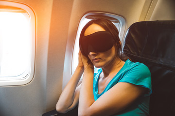 Young woman sleeping on a plane with black eye mask on her face - tired girl resting during a long...