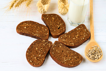 Rustic breakfast on a wooden background - sliced bread with seeds, sunflower seeds on a spoon, ears of wheat and a glass of milk