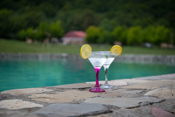 Glass of martini cocktail at swimming pool with ocean and palm tree background. A glass of blue martini cocktail welcome drink bar.Selective focus. season and holidays concept.