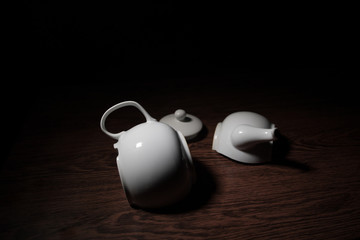 Naklejka na ściany i meble broken teapot on a dark toned foggy background. Pieces of ceramic teapot on wooden table.