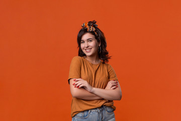 Smiling brunette woman in a t-shirt and beautiful headband standing isolated over orange background. Place for ad.