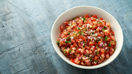 Mexican Tomato Salsa in white bowl with lime, red onion, jalapeno pepper, parsley and tortilla chips