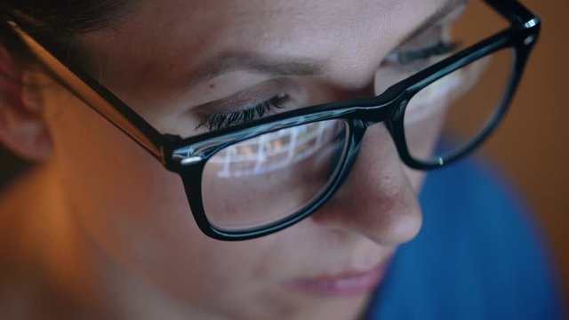 Woman in glasses looking on the monitor and surfing Internet. The monitor screen is reflected in the glasses