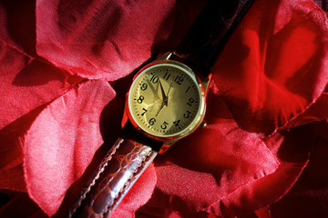 Gold and quartz watch with a leather strap on top of a pair of rose petals.