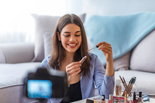Camera taking photo of woman putting make up on her face, using cosmetic brushes. Beauty blogger woman taking video at home, telling tutorial speech about cosmetic products.