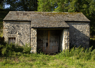 Fototapeta na wymiar A deserted and boarded up traditional Yorkshire Dales stone barn in a meadow just below Janet's Foss in Malham