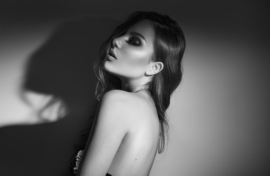 Sexy Young Woman black and white portrait. Seductive young woman in lingerie in darkness. Glamour lady with long hair posing in spotlight. Gorgeous seductive model girl with long hair b&w