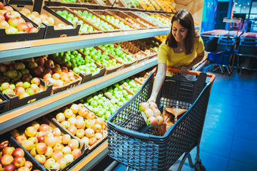 young pretty adult woman do shopping in grocery store buying apple