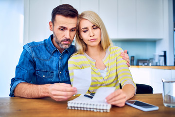 Sad couple looking sitting at home looking at bills and receipts worried about money