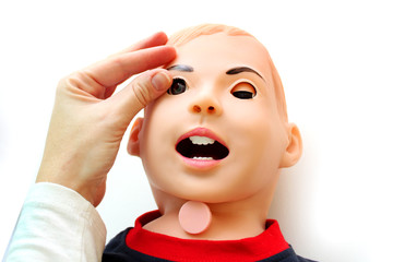 The head of a lying training dummy imitating a small child with an open mouth and female hand opening its eye