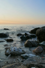 long exposure of the sea with rocks and sunset on the background