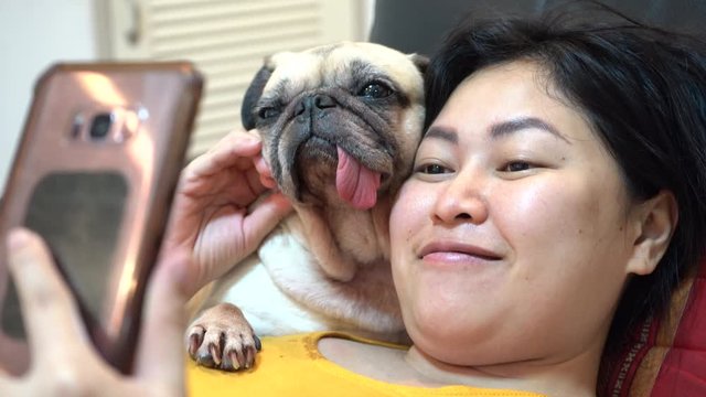 Beautiful young asian woman with cute pug dog taking selfie at home in 4K resolutions