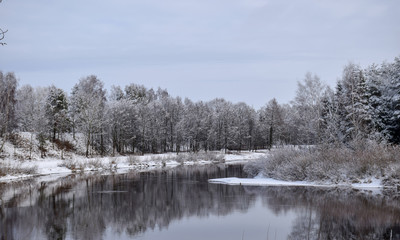 Obraz premium view of beautiful river winter day, snowy trees, many clouds, beautiful reflections, calm river water, Gauja river, Valmiera, Latvia