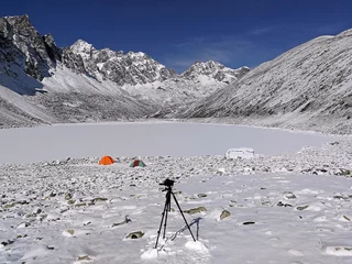 Fotobehang Camera on a tripod on the background of tent camp on the bank of a frozen lake in the Himalayan mountains  tourism and travel concept © kiwisoul