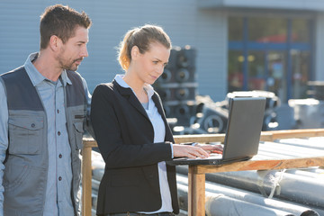 manager and worker looking at laptop in builders merchants yard