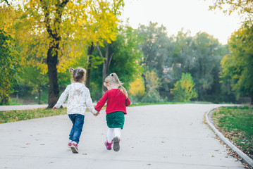 Fototapeta premium two little girls girlfriends playing at autumn city park holding hands