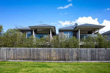 Two-storey residential houses with wooden fence facing vacant land with green grass. VIC Australia....