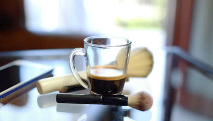 Cup of coffee with the phone and make-up set and brushes on the glass table